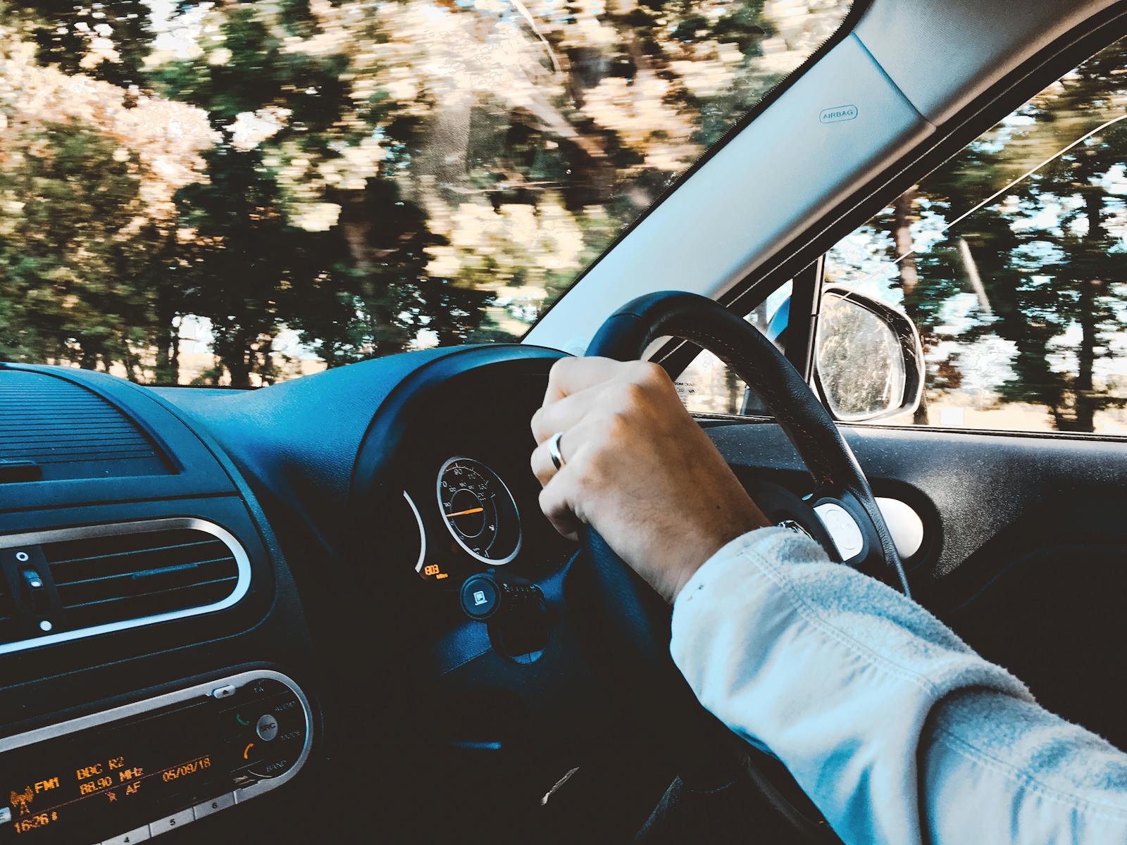 auto, Driver's hand on steering wheel of a modern car during a daytime drive through scenic outdoors.